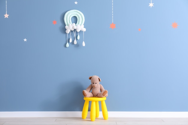 Stool with toy bear near color wall in children's room