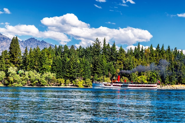 Stoomaangedreven schip op het meer Wakatipu, omgeven door naaldbossen in Queenstown, Nieuw-Zeeland