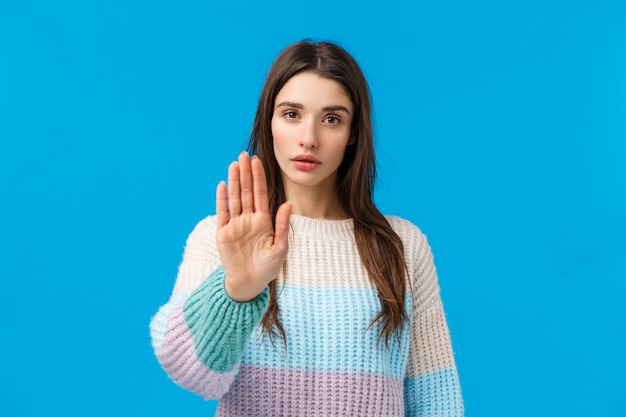 Stop alsjeblieft. Ernstig ogende assertieve en zelfverzekerde jonge aantrekkelijke vrouw trekt hand vooruit in verbod, afkeuring beweging, toon beperking vertellen genoeg, geen teken, staande blauw