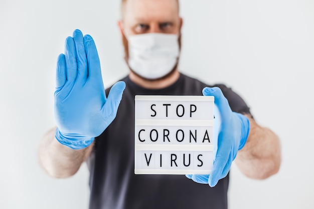 코로나 바이러스 개념을 중지하십시오. 텍스트 메시지 라이트 박스 코로나 바이러스 COVID-19 전염병 동안 라텍스 의료 장갑과 보호 마스크를 착용 한 사람의 손에 코로나 바이러스를 중지하십시오. 의료 및 안전