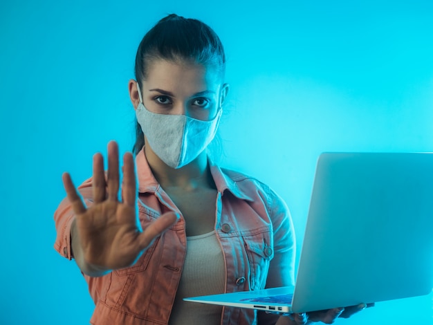 Stop coronavirus. Work at home. Woman with laptop on teal wall