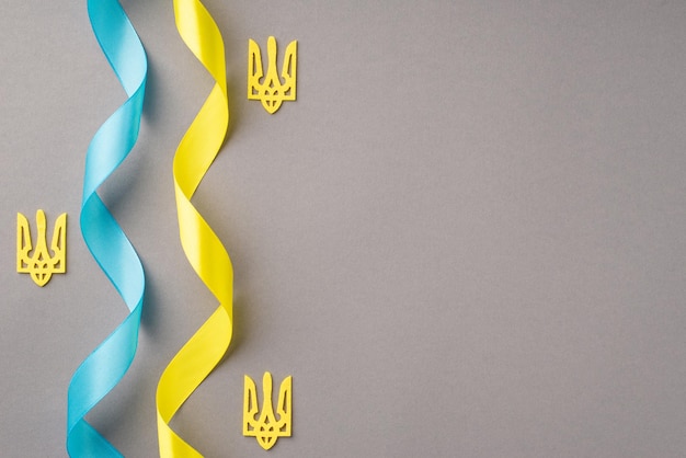 Stop de oorlog in Oekraïne concept Bovenaanzicht foto van nationale vlag kleuren gele en blauwe krullende linten en gouden drietand op geïsoleerde grijze achtergrond met lege ruimte
