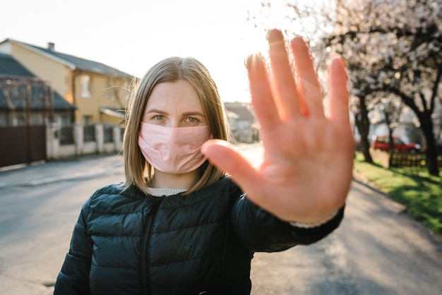 Stop de virusepidemische ziekten. Coronavirus. Een gezonde vrouw in een medisch beschermend masker dat een gebaarstop op straat toont. Bescherming van de gezondheid en preventie tijdens griep, besmettelijke uitbraak. Land.