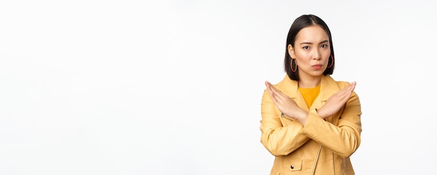 Stop gebaar Ernstige aziatische vrouw die arm kruist, verbiedt iets afkeer af te wijzen en actie af te keuren die op een witte achtergrond staat