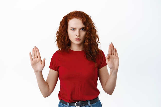 중지 흰색 배경에 서 있는 것을 금지하거나 거부하기 위해 손을 드는 블록 금기 제스처를 보여주는 진지하고 자신감 있는 빨간 머리 소녀