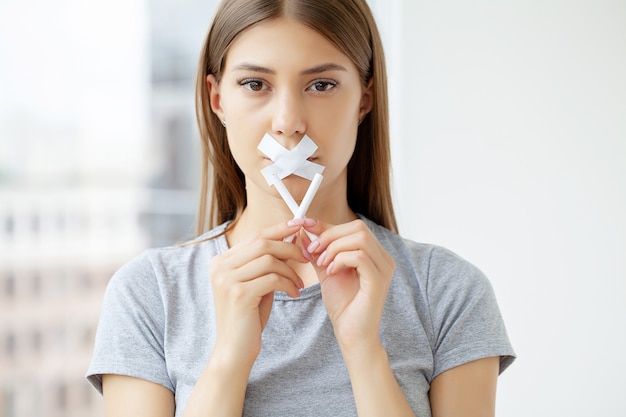 Stop met roken, een jonge vrouw met een verzegelde mond die een gebroken sigaret vasthoudt.