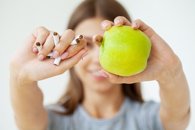 Stop smoking, woman holding broken cigarettes and green apple in hands.