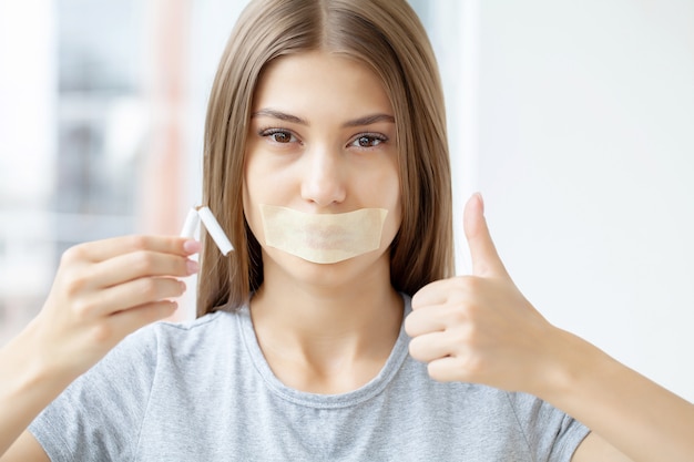 Stop smoking, a woman with a sealed mouth holding a broken cigarette