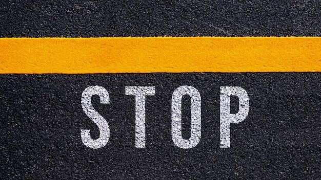 Stop text written and yellow line on the road in middle of the asphalt road Stop word on street