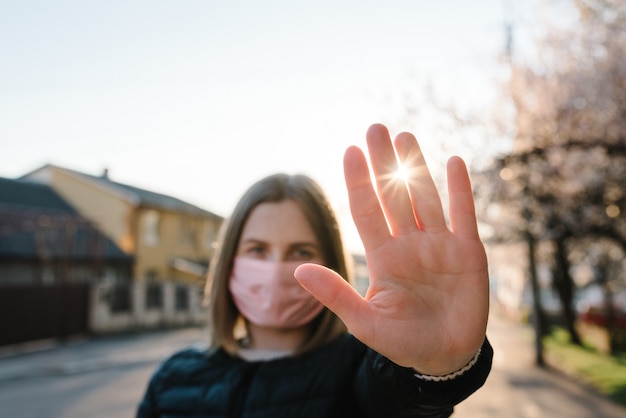 Stop the virus epidemic diseases. Coronavirus. A healthy woman in a medical protective mask showing a gesture stop on street. Health protection and prevention during flu, infectious outbreak. Country.