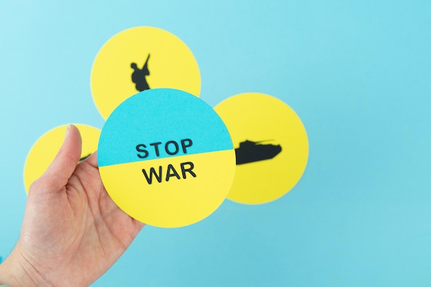 Фото Круг stop war с украинским флагом и сообщением stop war с одной стороны силуэт солдата и боевого танка на синем фоне скопируйте пространство