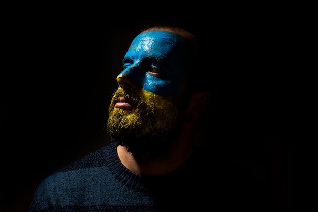 Stop war conflict between ukraine and russia portrait of a\
young man with his face painted in the blue and yellow colors of\
the flag looking left