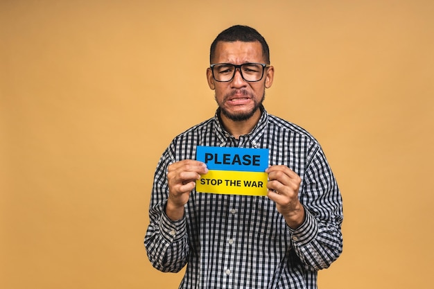 Photo stop war save ukraine portrait of sad negative african american black guy holding ukrainian flag isolated over beige background