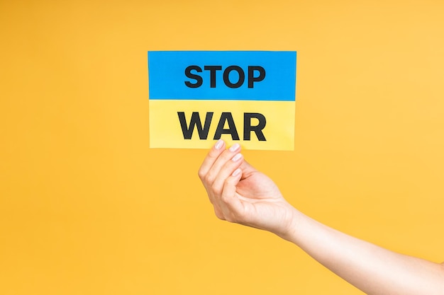 Stop war in Ukraine Close up photo woman's hand holding Ukrainian flag isolated over yellow pastel color background