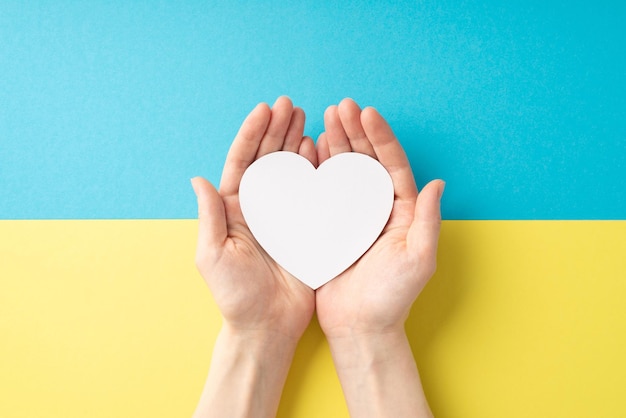 Stop the war in ukraine concept top overhead view photo of\
girl\'s hands holding white heart on the palms over national flag\
with copyspace