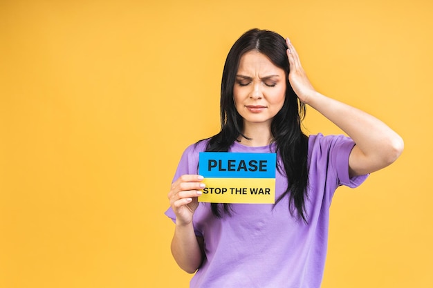 Stop war in Ukraine Portrait of sad agressive angry woman holding in hands Ukrainian flag isolated over yellow pastel color background