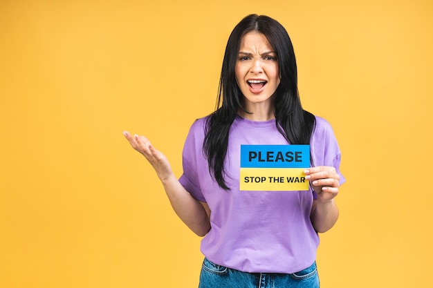 Stop war in Ukraine Portrait of sad agressive angry woman holding in hands Ukrainian flag isolated over yellow pastel color background