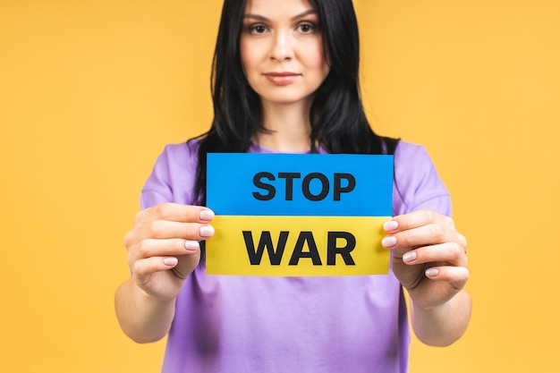 Stop war in Ukraine Portrait of sad agressive angry woman holding in hands Ukrainian flag isolated over yellow pastel color background