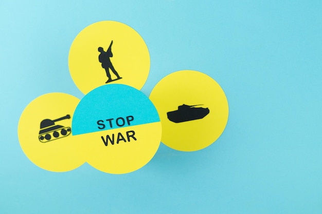 파란색 배경에 우크라이나 국기 복사 공간에 전쟁 중지 메시지가 있는 군인 및 전쟁 탱크의 실루엣이 있는 판지에 STOP WAR 노란색 원
