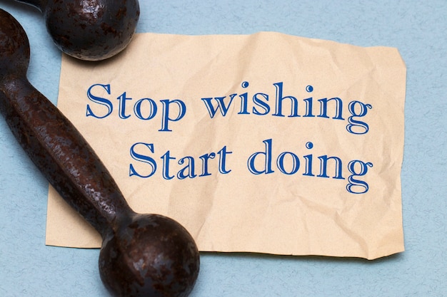 Stop wishing, start doing! Motivational phrase on a sheet of paper with dumbbells and measuring tape on blue background