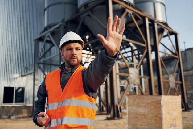 Stopgebaar tonen Bouwvakker in uniform is buiten in de buurt van de fabriek