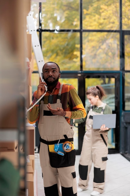 Storage room worker discussing goods stock supply with warehouse manager using landline phone working at inventory report Employee checking clients orders in storehouse preparing packages