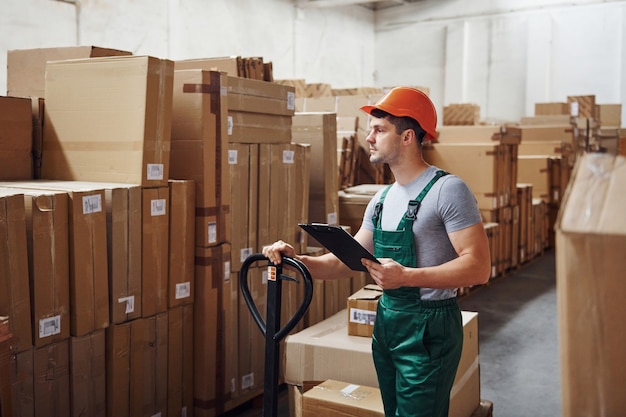 storage worker in green colored uniform and notepad in hands checks production.