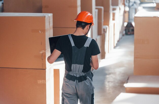 L'addetto allo stoccaggio in uniforme e un computer portatile moderno nelle mani controlla la produzione.