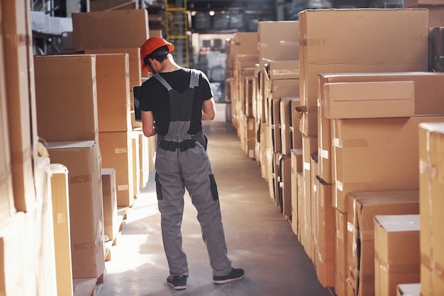 Storage worker in uniform and modern laptop in hands checks production.