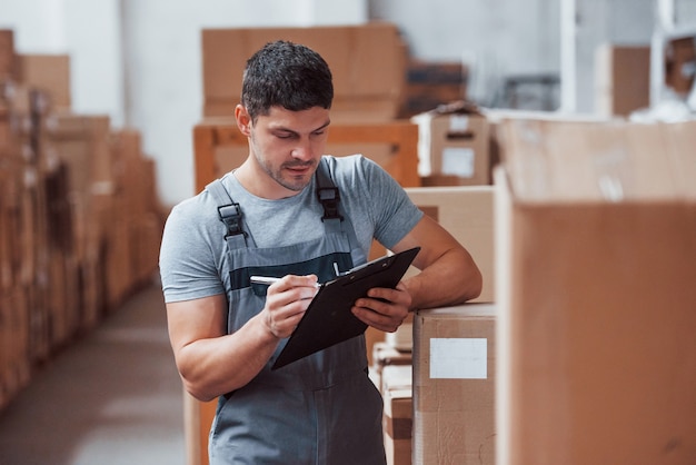 Storage worker in uniform and notepad in hands checks production.