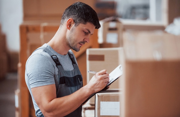 Storage worker in uniform and notepad in hands checks production.