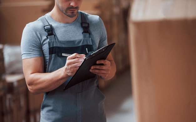 Storage worker in uniform and notepad in hands checks production.