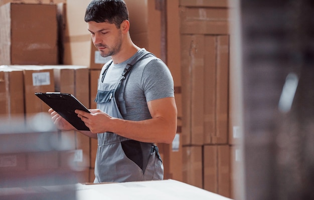 Storage worker in uniform and notepad in hands checks production.