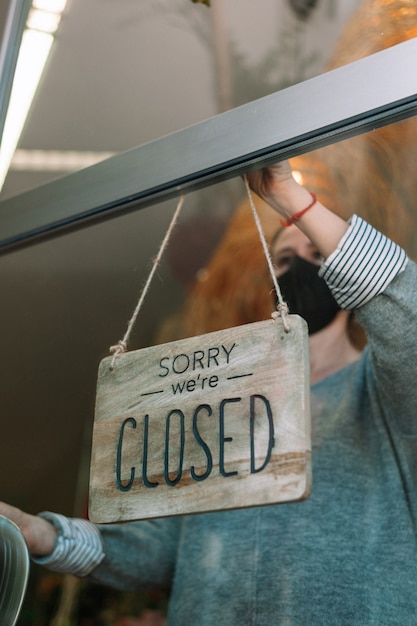 Store owner wearing mask turning open sign broad through the door glass and ready toservice