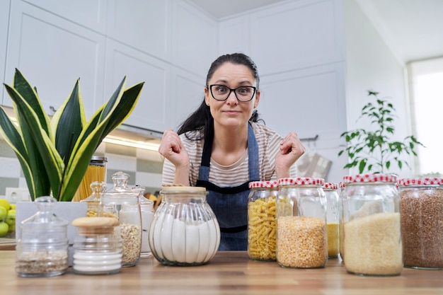 Storing food in kitchen woman with jars and containers talking and looking at camera