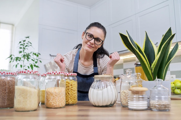 Storing food in kitchen woman with jars and containers talking and looking at camera