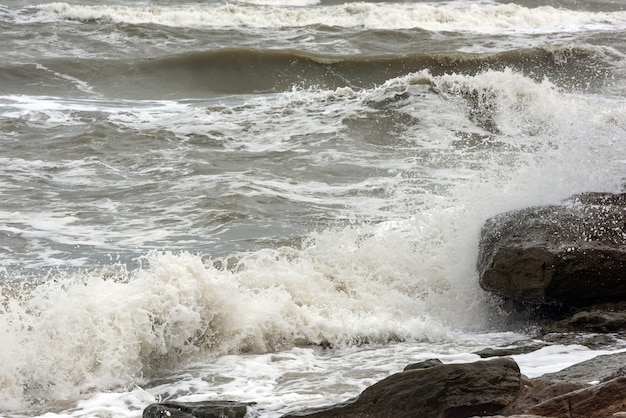 Storm in the sea, big foamy waves crash on rocks