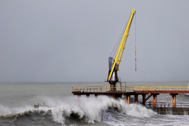 Storm in the sea. A large splashing wave hits the breakwater. Industrial crane at sea