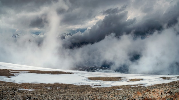 Storm on the top of a mountain. Wonderful dramatic landscape with big snowy mountain peaks above low clouds. Atmospheric large snow mountain tops in cloudy sky.