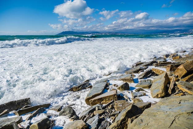 Storm waves in white foam break on the beach strewn with fragments of yellowish Sandstone rocks