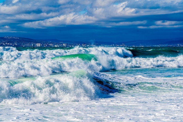 Storm waves in white foam rush in rows along the Tsemesskaya Bay Blue sky and green sea