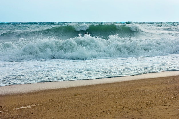 Stormachtige zee en blauwe lucht, witte zee schuim op een geel zandstrand.