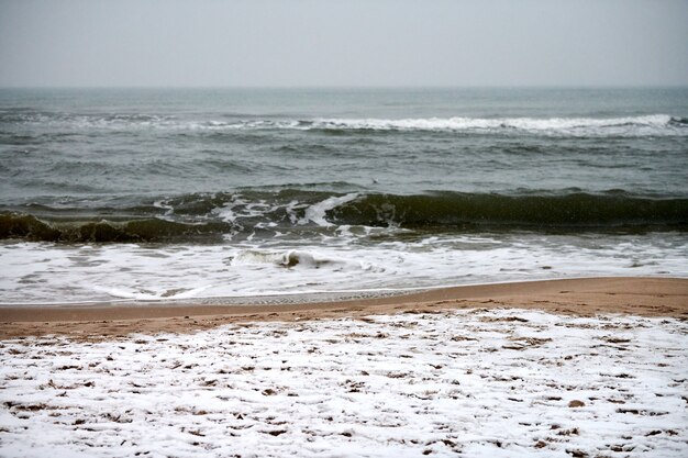 Stormy Baltic Sea winter landscape. Bubbling and foaming sea waves, and sandy beach covered with snow. Silence and solitude.