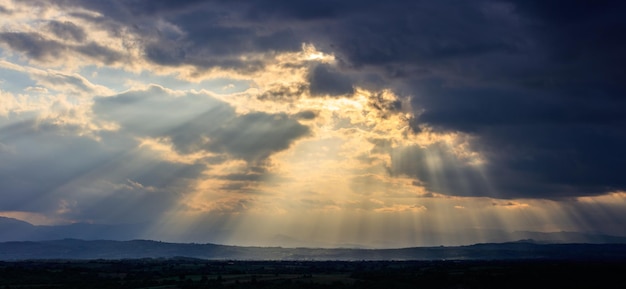 Stormy clouds with radiating sunbeams above countryside