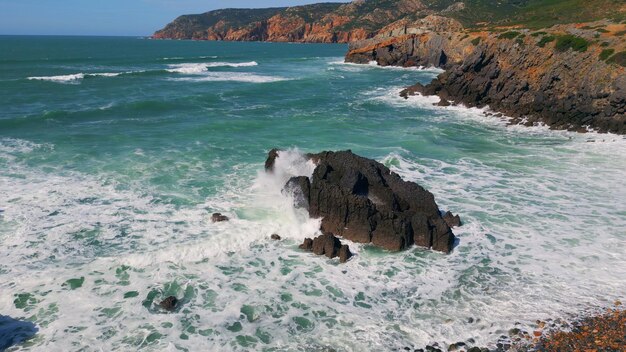 Foto acqua di mare tempestosa che spruzza sulle rocce costiere costa rocciosa del drone di una giornata di sole