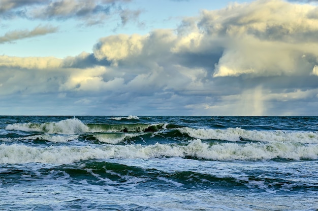 Stormy sea with foamy waves under low floating amazing clouds