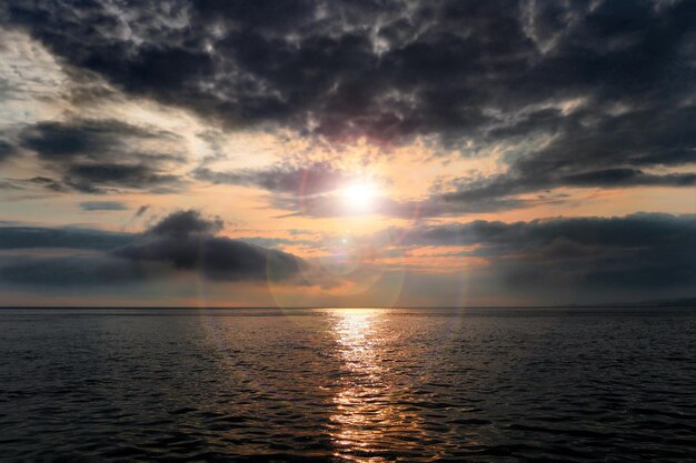 바다 위의 폭풍우 치는 일몰 우울한 구름을 통해 태양 광선 물에 태양의 반사