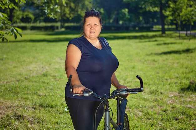 Stout mature woman on bike ride in public park on sunny summer day