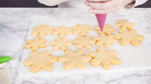 Stp by step. Icing snowflake shaped sugar cookies with pink royal icing.