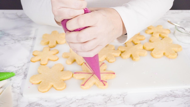 Stp by step. Icing snowflake shaped sugar cookies with pink royal icing.